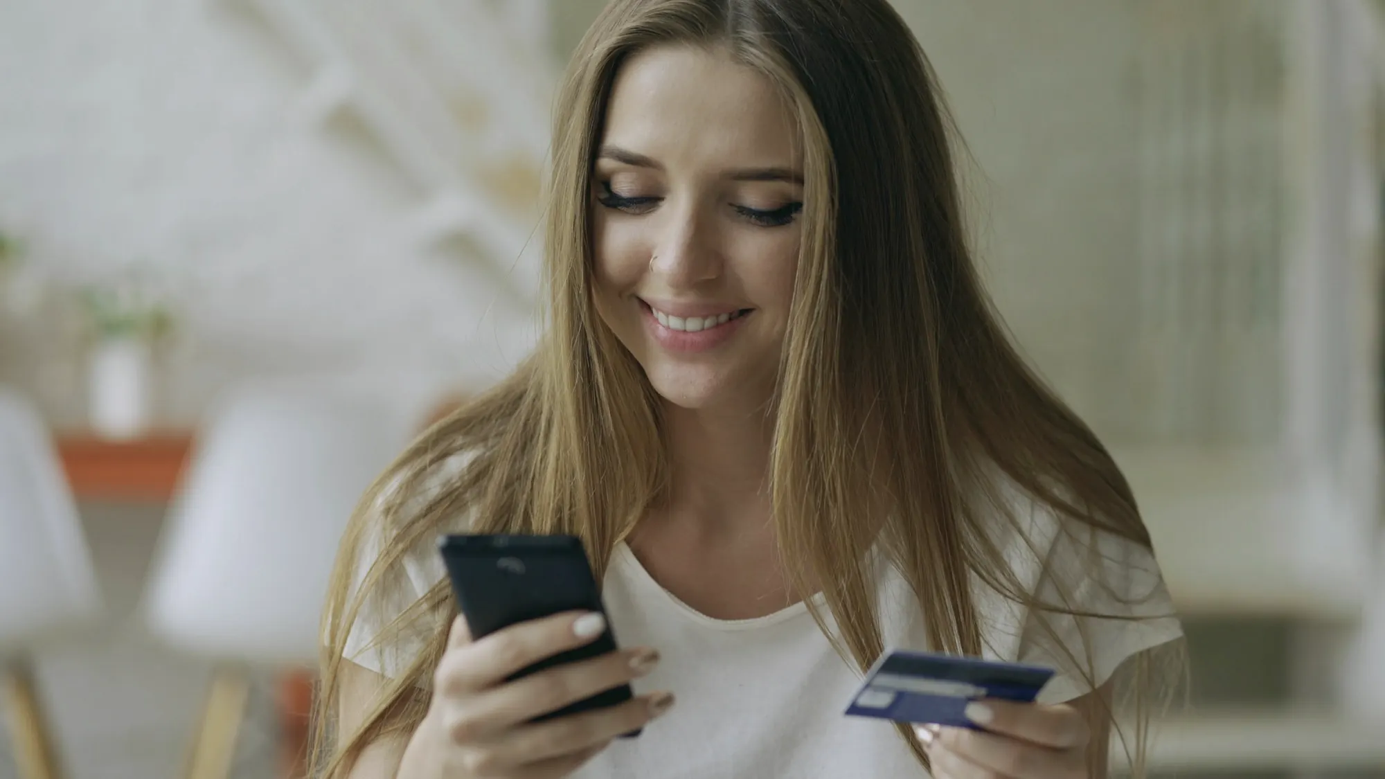 A woman smiling at her phone while holding a payment card
